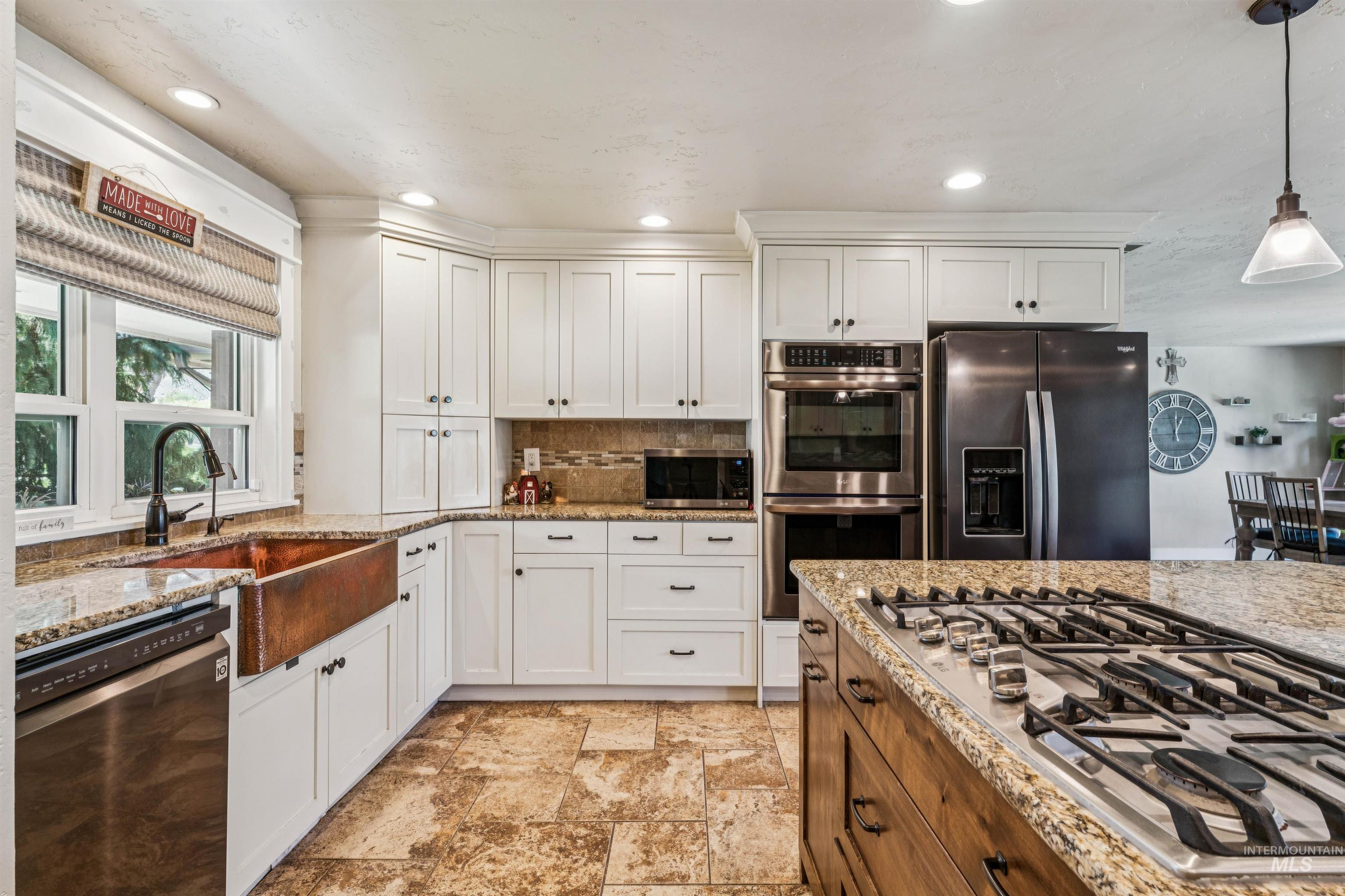 1050 West South Slope Road Emmett, ID 83617 - Photo 13 of 49 Two tone kitchen with stainless steel appliances, dual tone cabinetry, hanging light fixtures, and light stone countertops