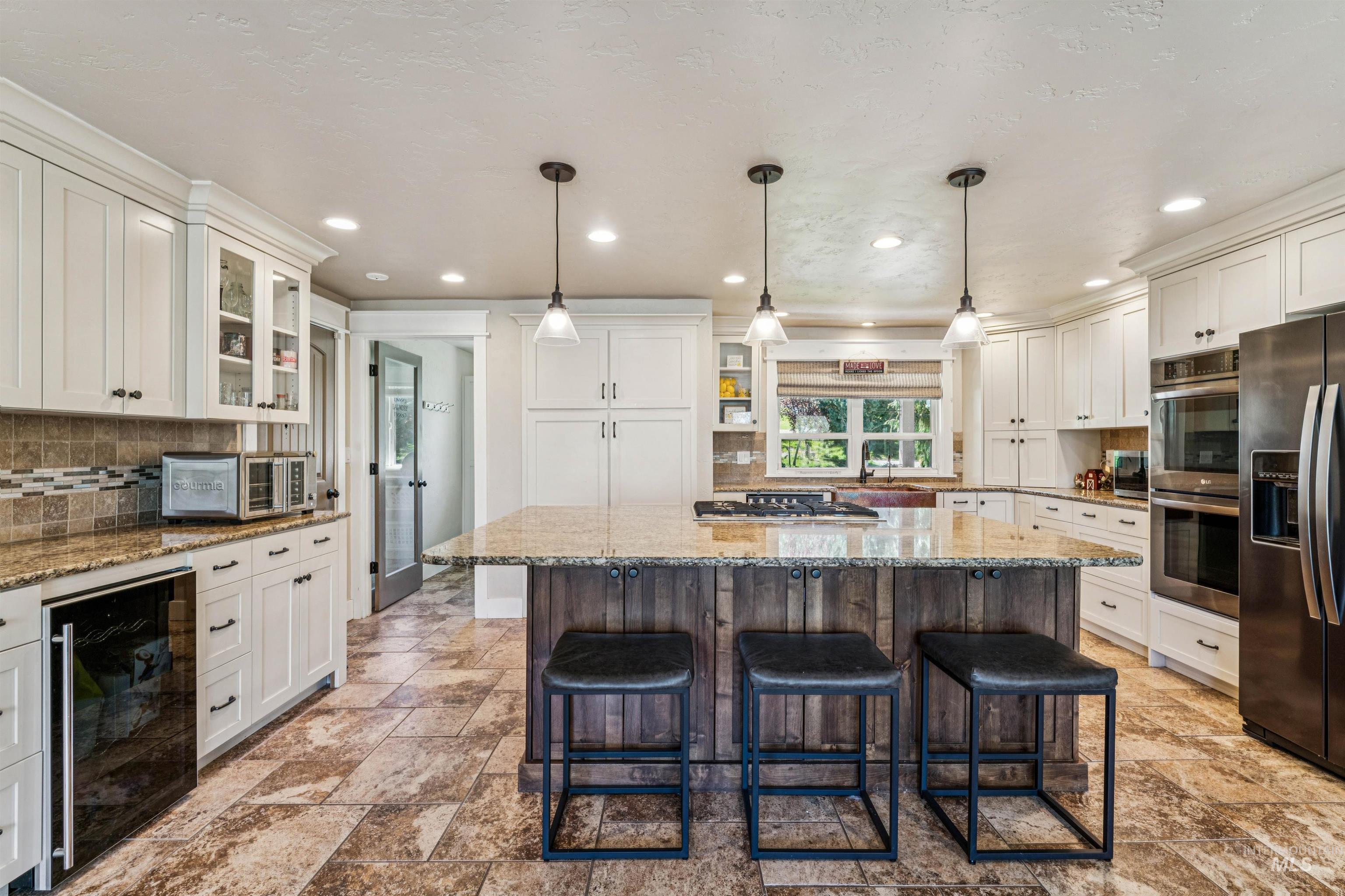 1050 West South Slope Road Emmett, ID 83617 - Photo 14 of 49 Dual tone kitchen with a kitchen breakfast bar, light stone counters, beverage cooler, stainless steel appliances, and two tone cabinets