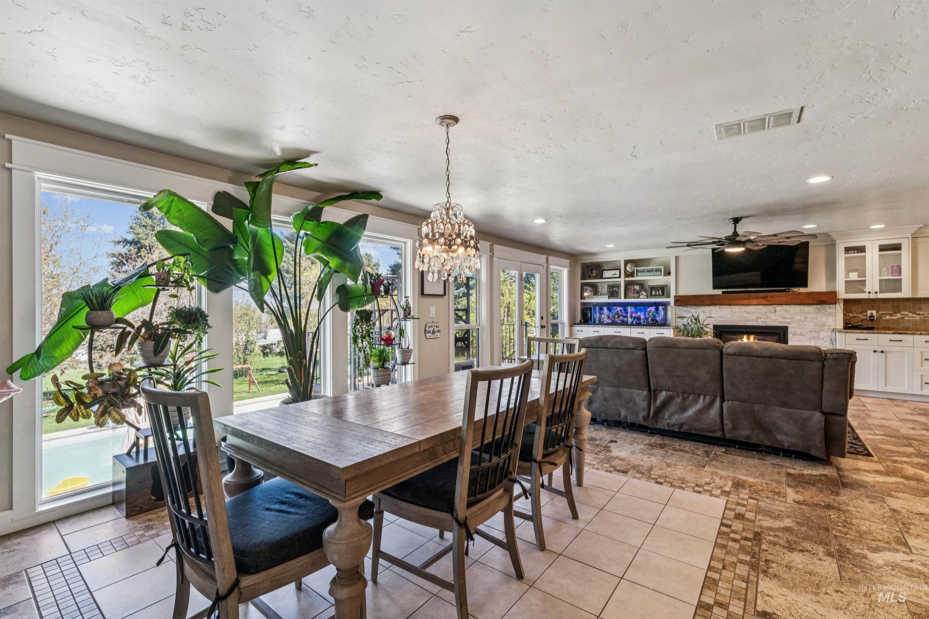 1050 West South Slope Road Emmett, ID 83617 - Photo 10 of 49 Dining space with ceiling fan, inlaid floor details, a lit fireplace, light tile patterned floors, and a textured ceiling