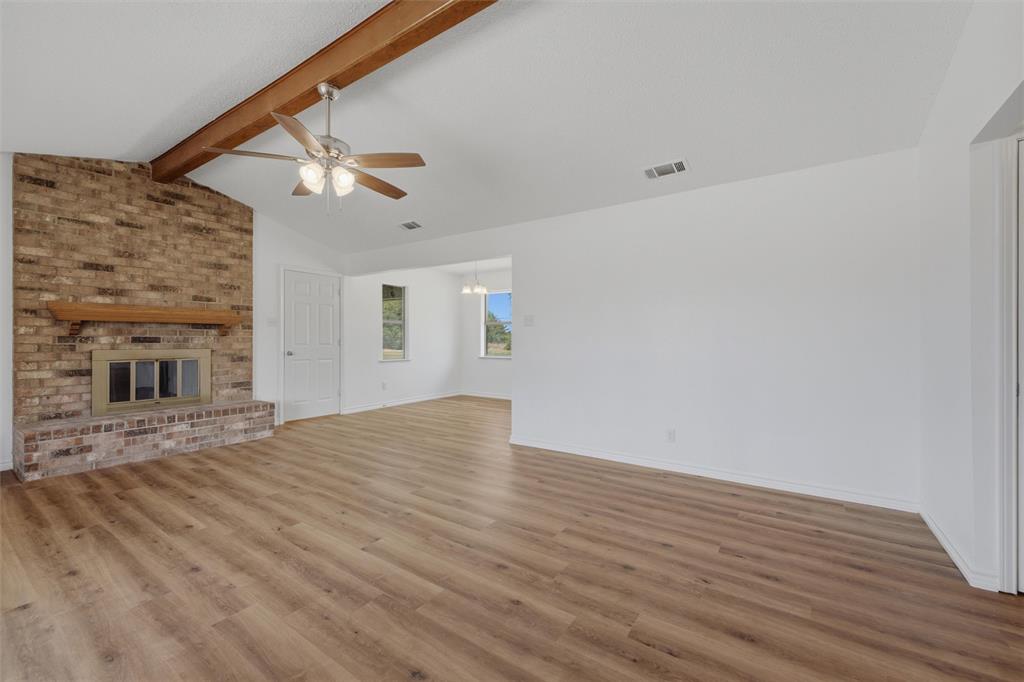124 Prairie Creek Road Red Oak, TX 75154 - Photo 4 of 17 Spacious living area showcasing wood-finish flooring, exposed wooden beam ceiling detail, and a brick fireplace with glass doors