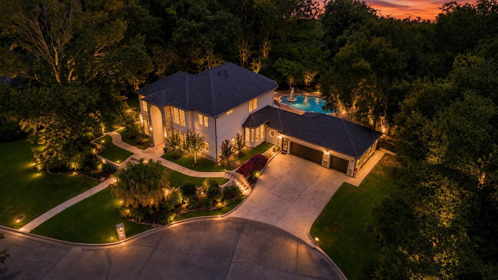 1810 Woerner Road Houston, TX 77090 - Photo 2 of 39 This stunning two-story home is beautifully illuminated at dusk, featuring a spacious driveway, lush landscaping, and a large pool surrounded by trees, offering a luxurious and private retreat.