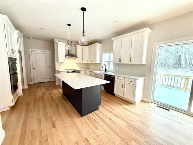 a large kitchen with kitchen island a stove a sink dishwasher a refrigerator and white cabinets with wooden floor