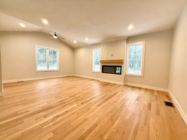 an empty room with wooden floor fireplace and windows