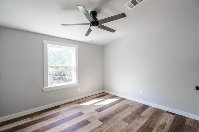 an empty room with wooden floor ceiling fan and windows