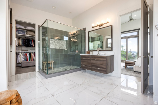 140 West Vista Road Kamas, UT 84036 - Photo 45 of 101 White tile flooring, glass-enclosed shower with pebble floor, floating wood-finish vanity with countertop, and an adjacent walk-in closet