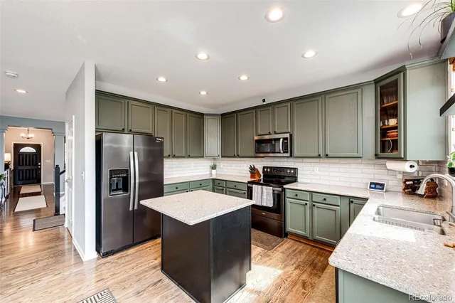 a kitchen with stainless steel appliances kitchen island granite countertop a refrigerator a sink a stove top oven and a center island