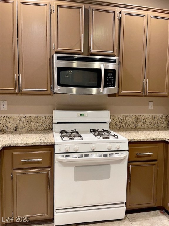 7640 Sierra Paseo Lane Las Vegas, NV 89128 - Photo 4 of 49 Kitchen with white gas range, stainless steel microwave, light stone countertops, and light tile patterned floors