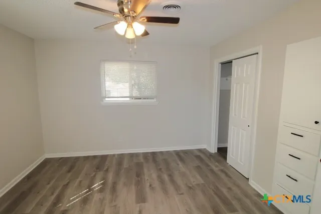 an empty room with a chandelier fan and wooden floor