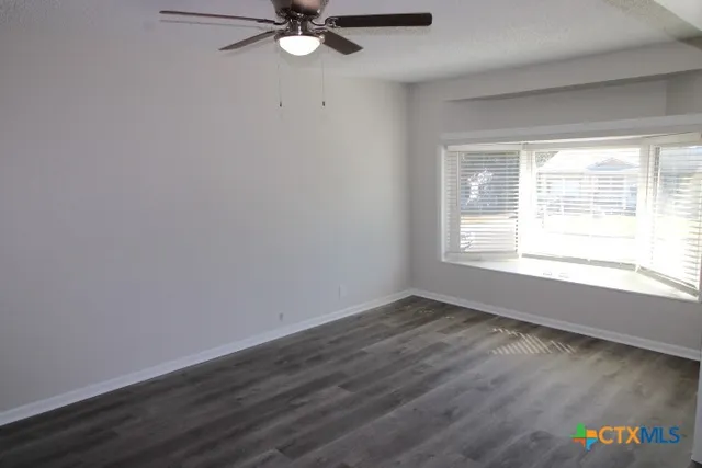 an empty room with wooden floor fan and windows