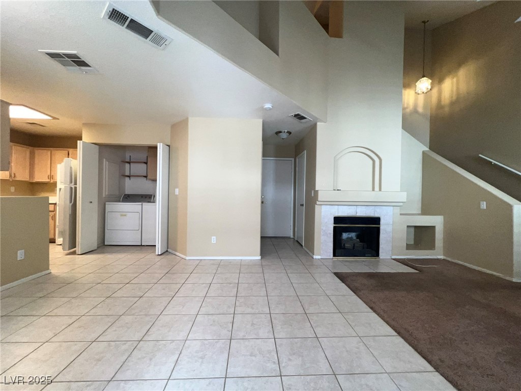 8028 Desire Drive Las Vegas, NV 89128 - Photo 2 of 15 Unfurnished living room featuring light tile patterned flooring, a tile fireplace, separate washer and dryer, and a high ceiling