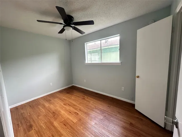 an empty room with wooden floor ceiling fan and windows