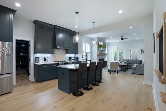 a kitchen with stainless steel appliances kitchen island granite countertop a refrigerator a sink dishwasher a dining table and chairs with wooden floor