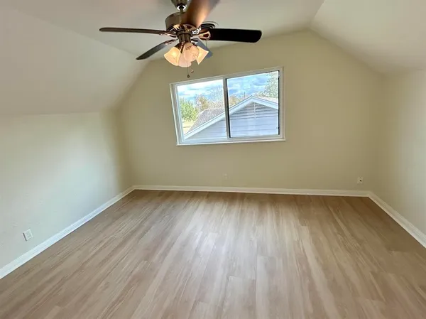 an empty room with wooden floor ceiling fan and windows