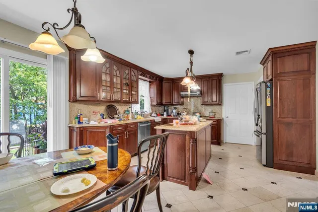 a kitchen with stainless steel appliances granite countertop a refrigerator a sink dishwasher a stove and a dining table with wooden floor