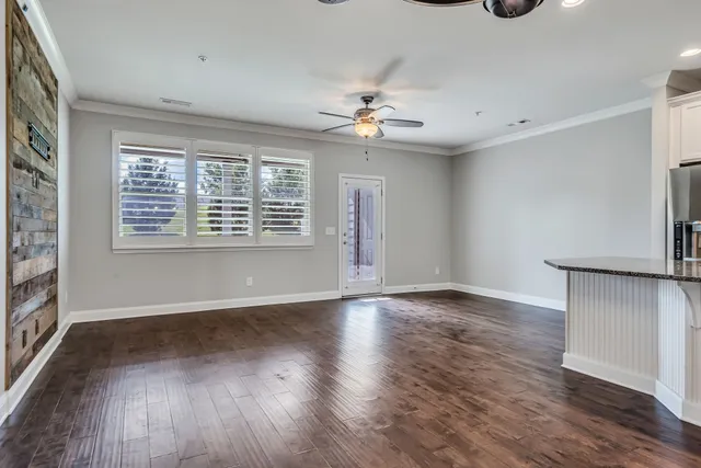 an empty room with wooden floor chandelier fan and windows