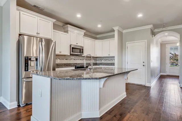 a kitchen with stainless steel appliances granite countertop a refrigerator a stove a sink and white cabinets with wooden floor