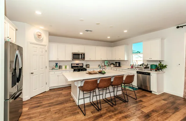 a kitchen with stainless steel appliances a stove a sink a refrigerator white cabinets and wooden floor