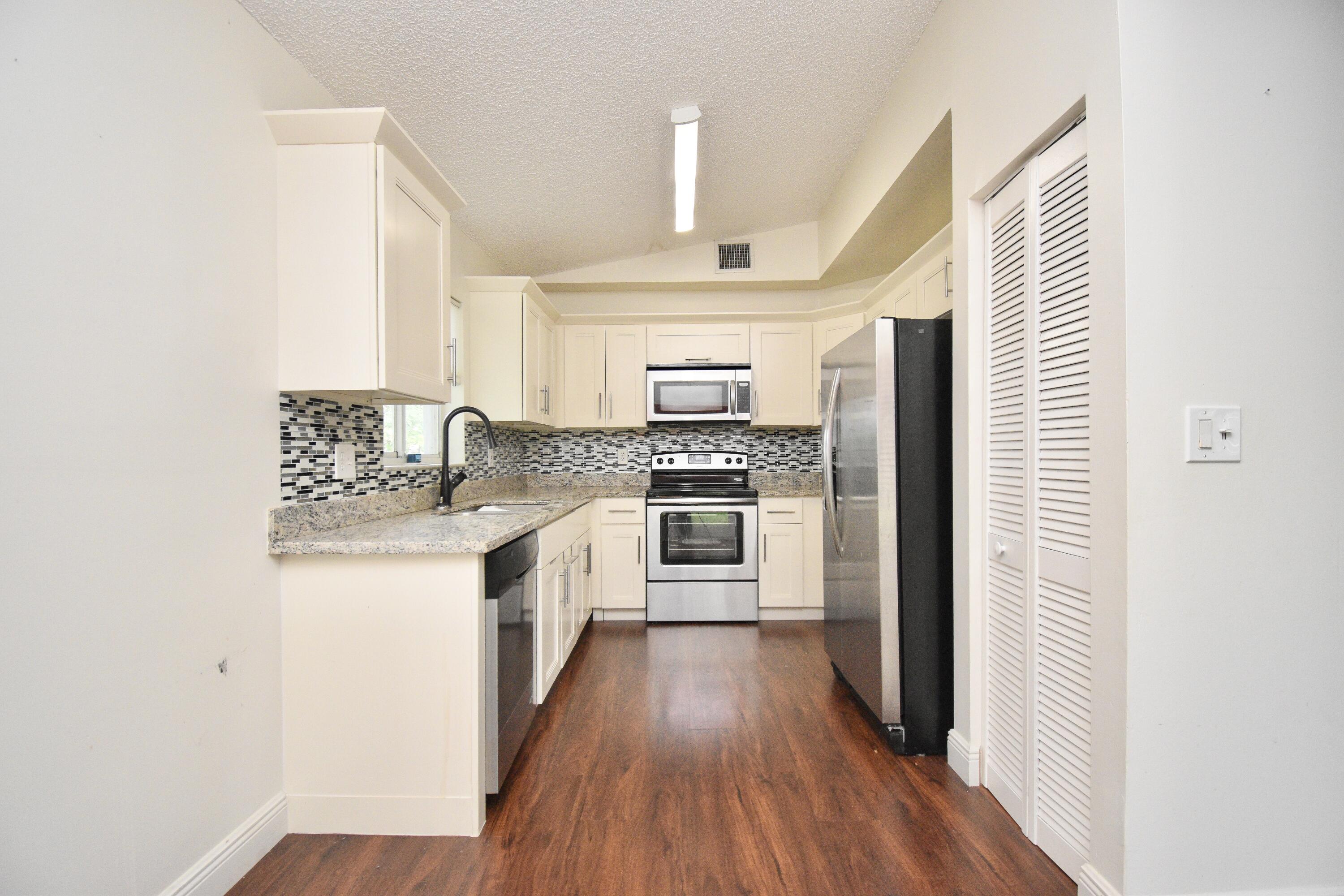 6053 Old Court Road, Unit 308 Boca Raton, FL 33433 - Photo 4 of 22 a kitchen with granite countertop a refrigerator a sink dishwasher a stove and white cabinets with wooden floor