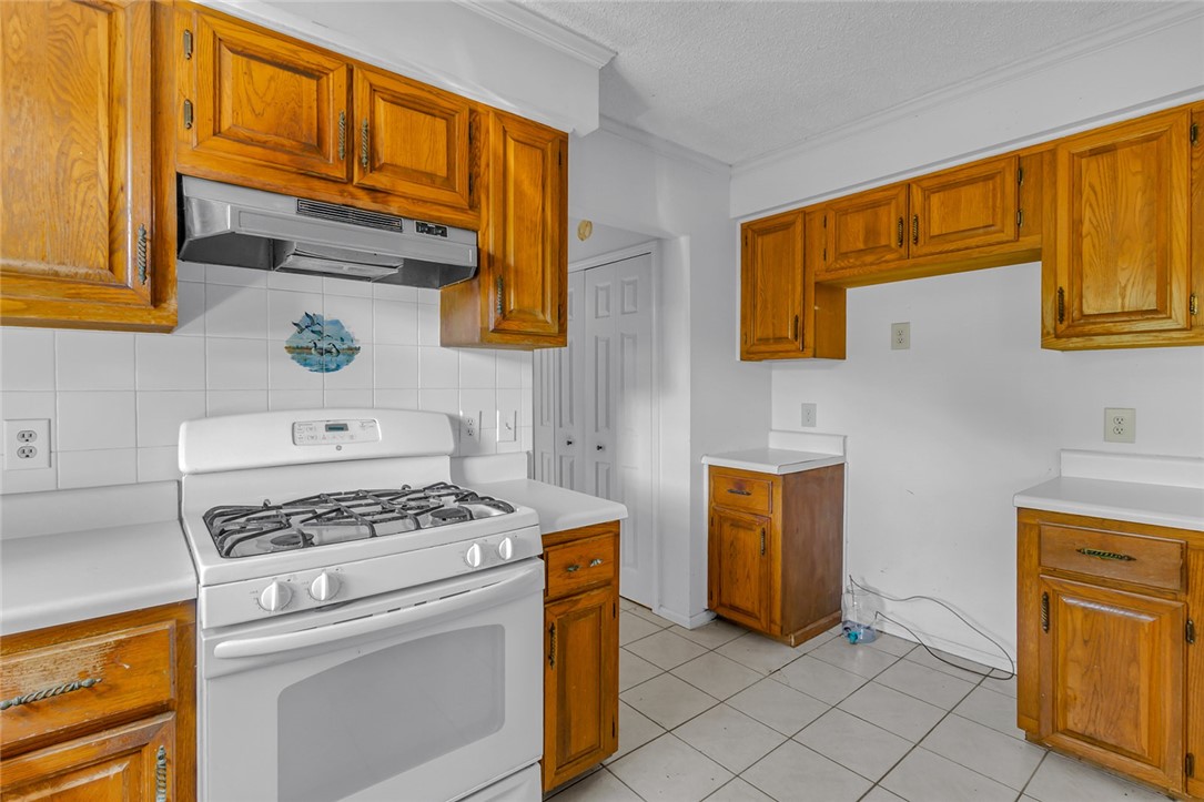 148 Denver Road Heathsville, VA 22473 - Photo 28 of 50 Kitchen featuring white gas range oven, light countertops, brown cabinets, under cabinet range hood, and light tile patterned floors