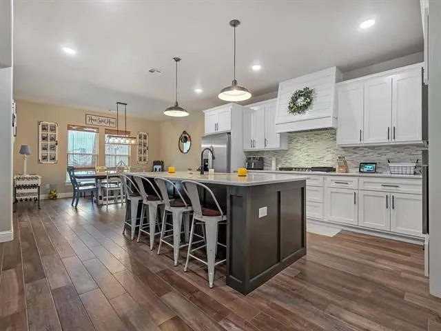 a kitchen with stainless steel appliances granite countertop a stove a sink dishwasher and a dining table with wooden floor