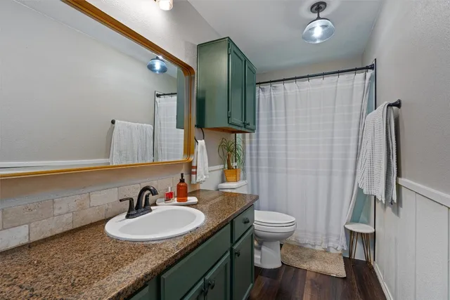 a bathroom with a granite countertop sink a toilet a mirror and shower