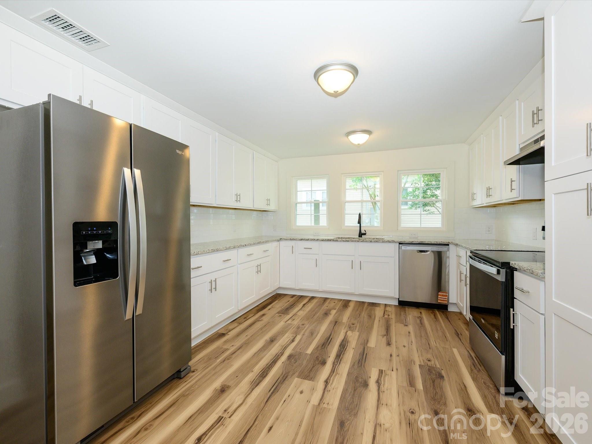 156 Hartsell School Road Southwest Concord, NC 28027 - Photo 10 of 28 a large kitchen with a refrigerator a sink dishwasher a stove and white countertops with wooden floor