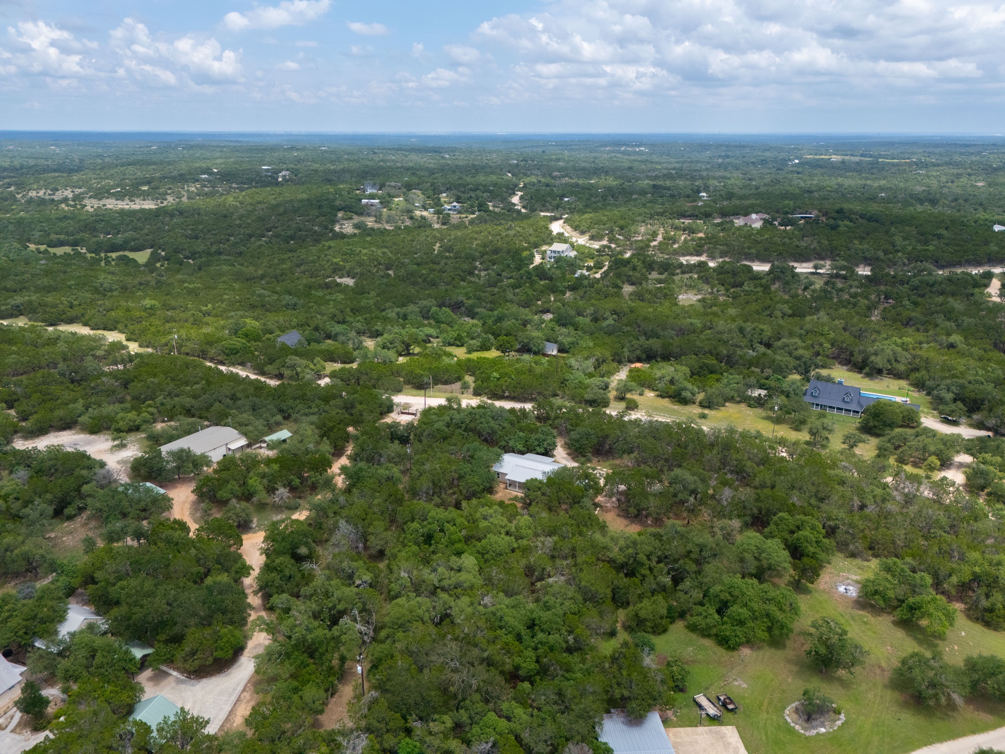 231 North Rainbow Ranch Road Wimberley, TX 78676 - Photo 38 of 40 An aerial perspective reveals a vast, tree-filled landscape with scattered residences and a clear blue sky above.