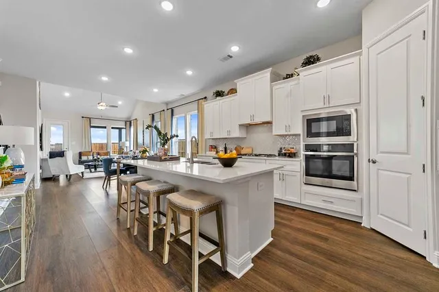 a kitchen with stainless steel appliances granite countertop a stove top oven a refrigerator a sink and a dining table with wooden floor