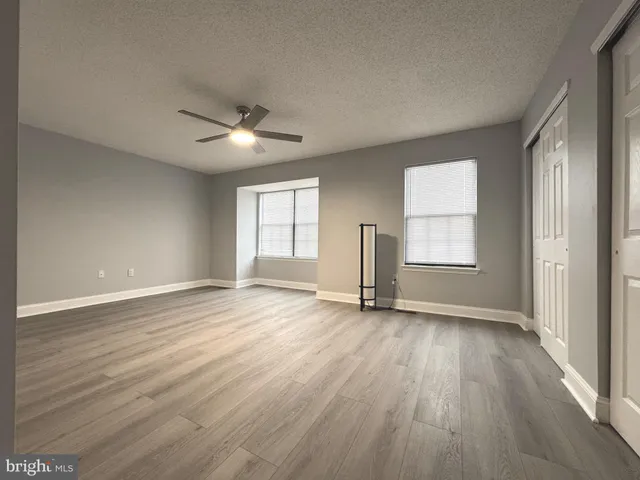 an empty room with wooden floor chandelier fan and windows