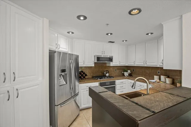 a kitchen with stainless steel appliances granite countertop a refrigerator a sink a stove and white cabinets with wooden floor