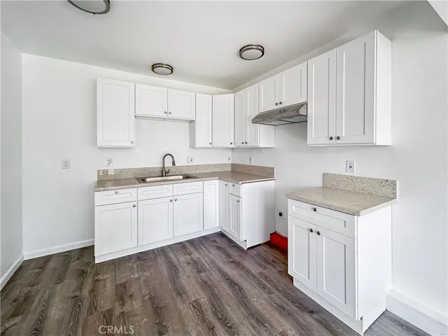 a kitchen with a sink dishwasher and white cabinets with wooden floor