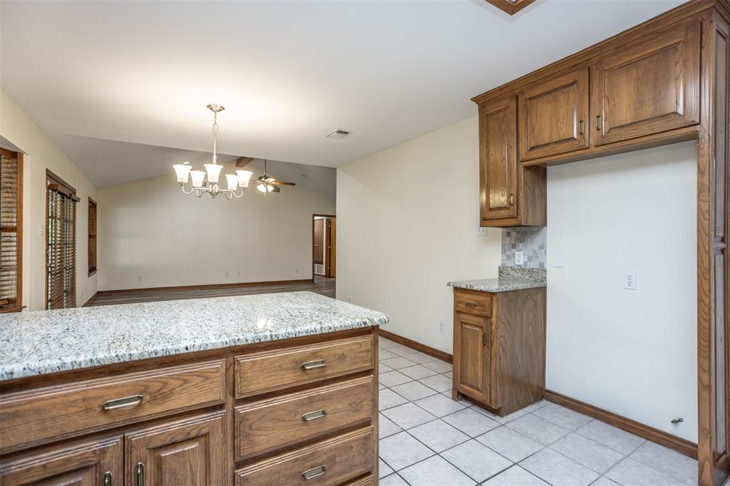292 Old Spanish Trail Valley View, TX 76272 - Photo 20 of 40 Kitchen featuring a chandelier, light stone counters, brown cabinets, light tile patterned floors, and vaulted ceiling