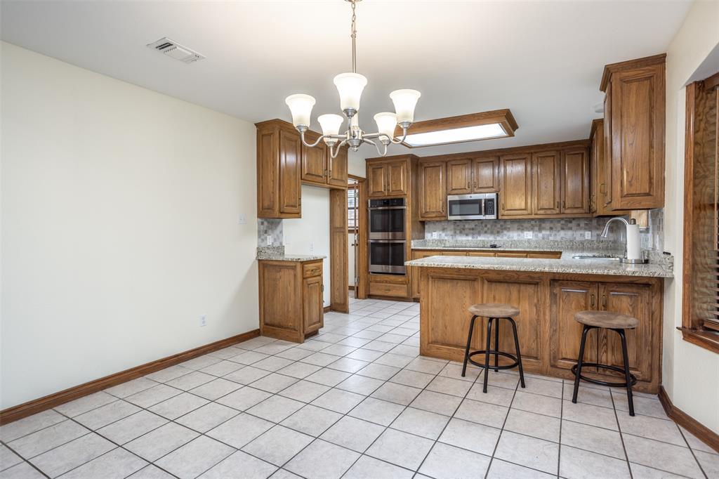 292 Old Spanish Trail Valley View, TX 76272 - Photo 21 of 40 Kitchen with appliances with stainless steel finishes, brown cabinetry, a chandelier, tasteful backsplash, and a peninsula
