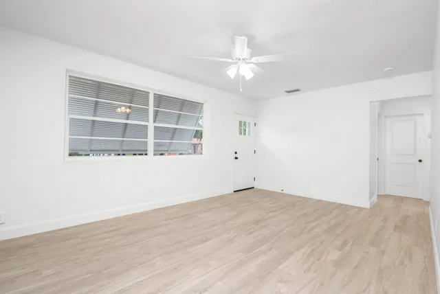 an empty room with wooden floor fan and windows