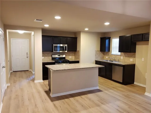 a kitchen with stainless steel appliances kitchen island granite countertop a stove a sink and a refrigerator
