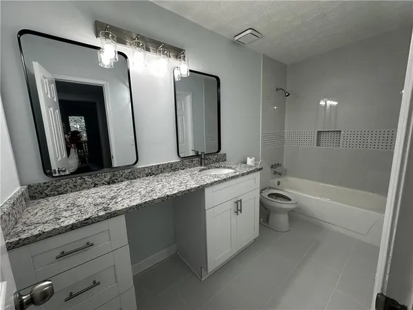 a bathroom with a granite countertop double vanity sink and mirror with bathtub