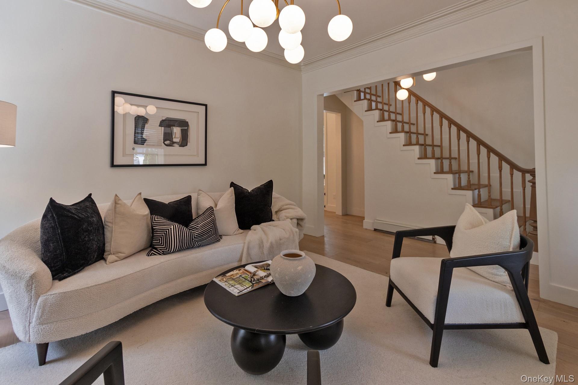 114 Rombout Avenue Beacon, NY 12508 - Photo 7 of 32 Open-concept living area featuring light wood-finish flooring, a contemporary chandelier with multiple globe lights, and an elegant staircase with wood newel posts and balusters