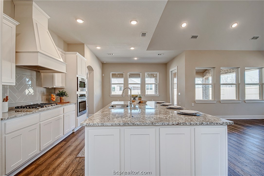 a kitchen with granite countertop kitchen island stainless steel appliances a stove a sink a oven and a granite counter tops with white cabinets