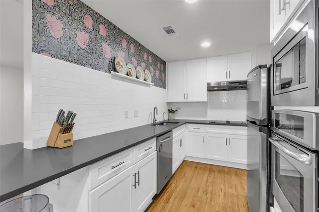 a kitchen with a sink dishwasher a stove and white cabinets with wooden floor
