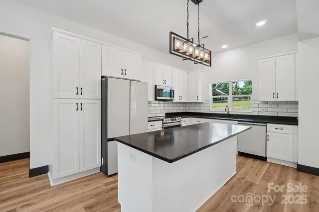 a kitchen with stainless steel appliances granite countertop a refrigerator a sink dishwasher a dining table and chairs with wooden floor