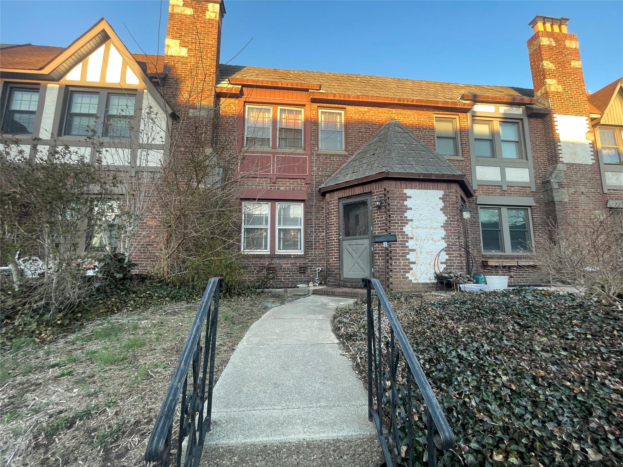View of front of property with brick siding, a chimney, and a shingled roof