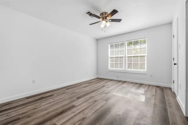 an empty room with wooden floor ceiling fan and windows