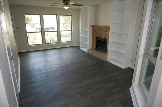 an empty room with wooden floor fireplace and windows