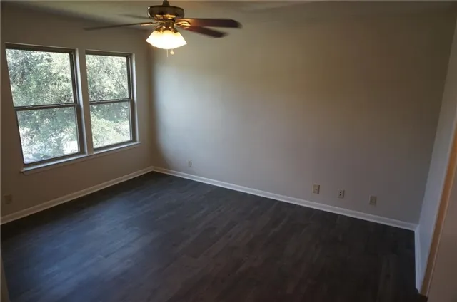 an empty room with wooden floor fan and windows