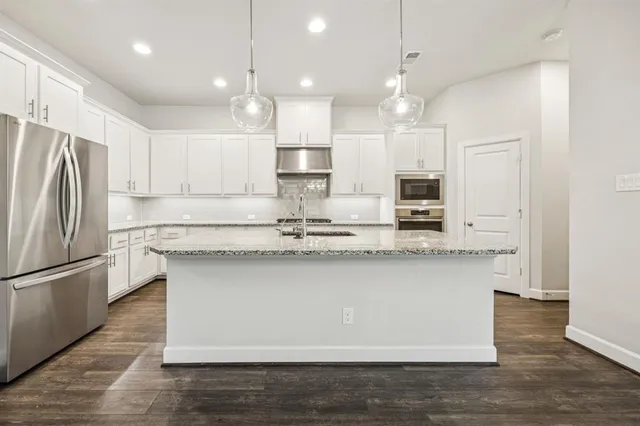 a kitchen with stainless steel appliances granite countertop a sink a stove a refrigerator and island with wooden floor