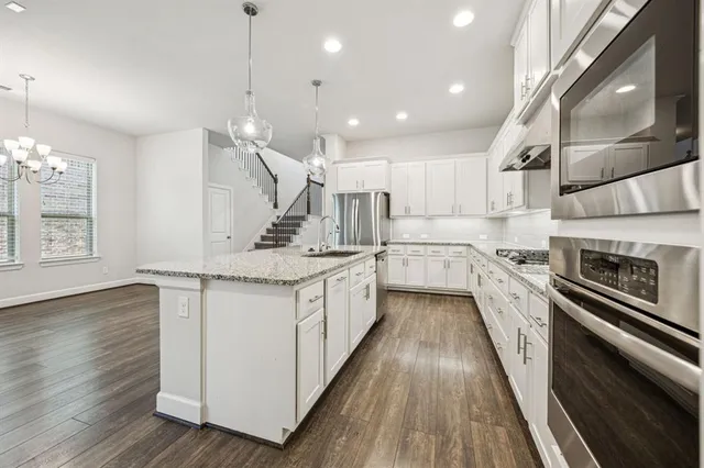 a large kitchen with granite countertop a large counter top a sink stainless steel appliances and cabinets