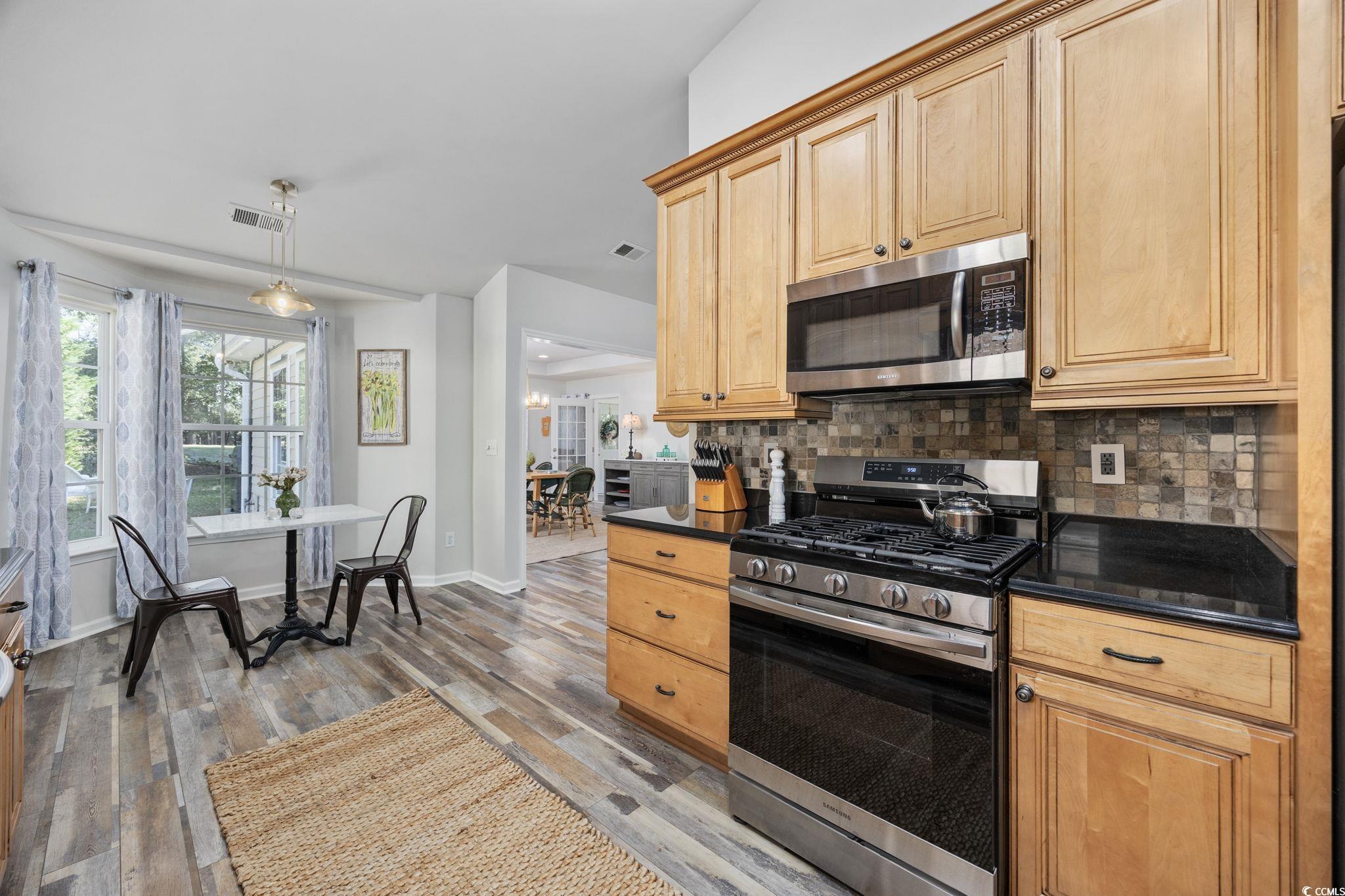 4618 Fringetree Drive Murrells Inlet, SC 29576 - Photo 8 of 40 Kitchen featuring stainless steel appliances, backsplash, light wood-style floors, decorative light fixtures, and dark stone countertops