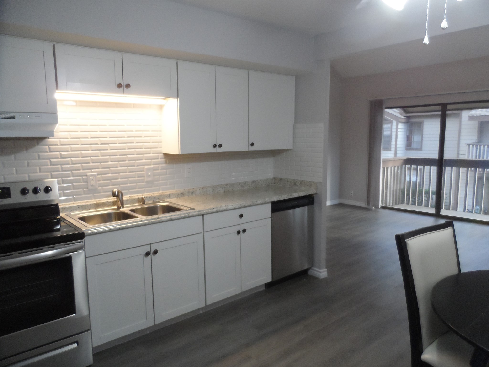 12900 Walden Road, Unit 618F Montgomery, TX 77356 - Photo 3 of 12 Updated kitchen with white cabinetry, granite countertops, stainless steel appliances, and modern tile backsplash—open to dining and living areas.