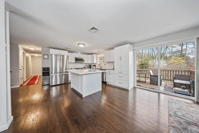 a living room with stainless steel appliances kitchen island wooden floor and large windows