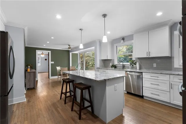 a kitchen with stainless steel appliances granite countertop a stove a refrigerator a sink dishwasher and a dining table with wooden floor